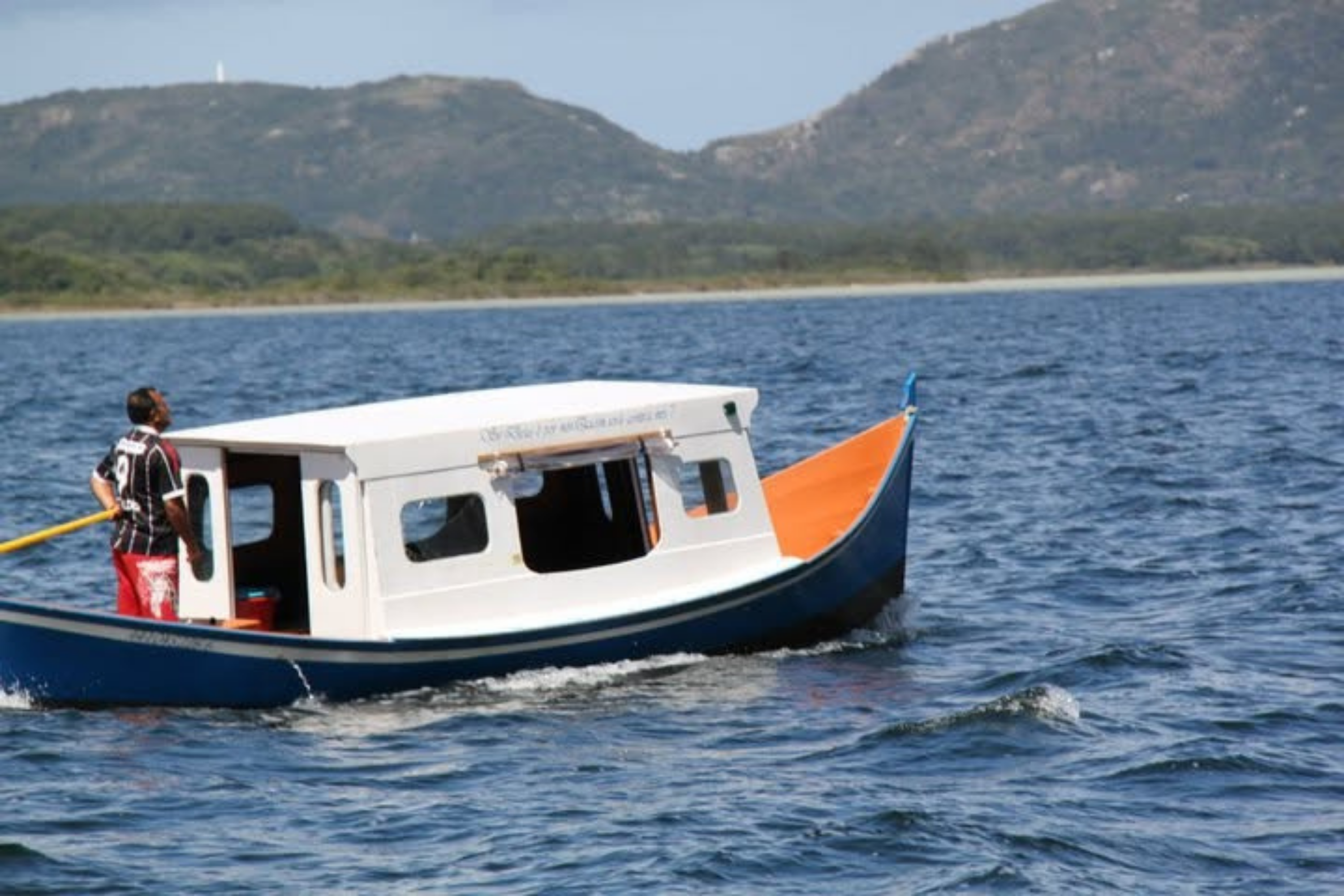 Barco navegando junto à costa de Santa Catarina, com as montanhas ao fundo.